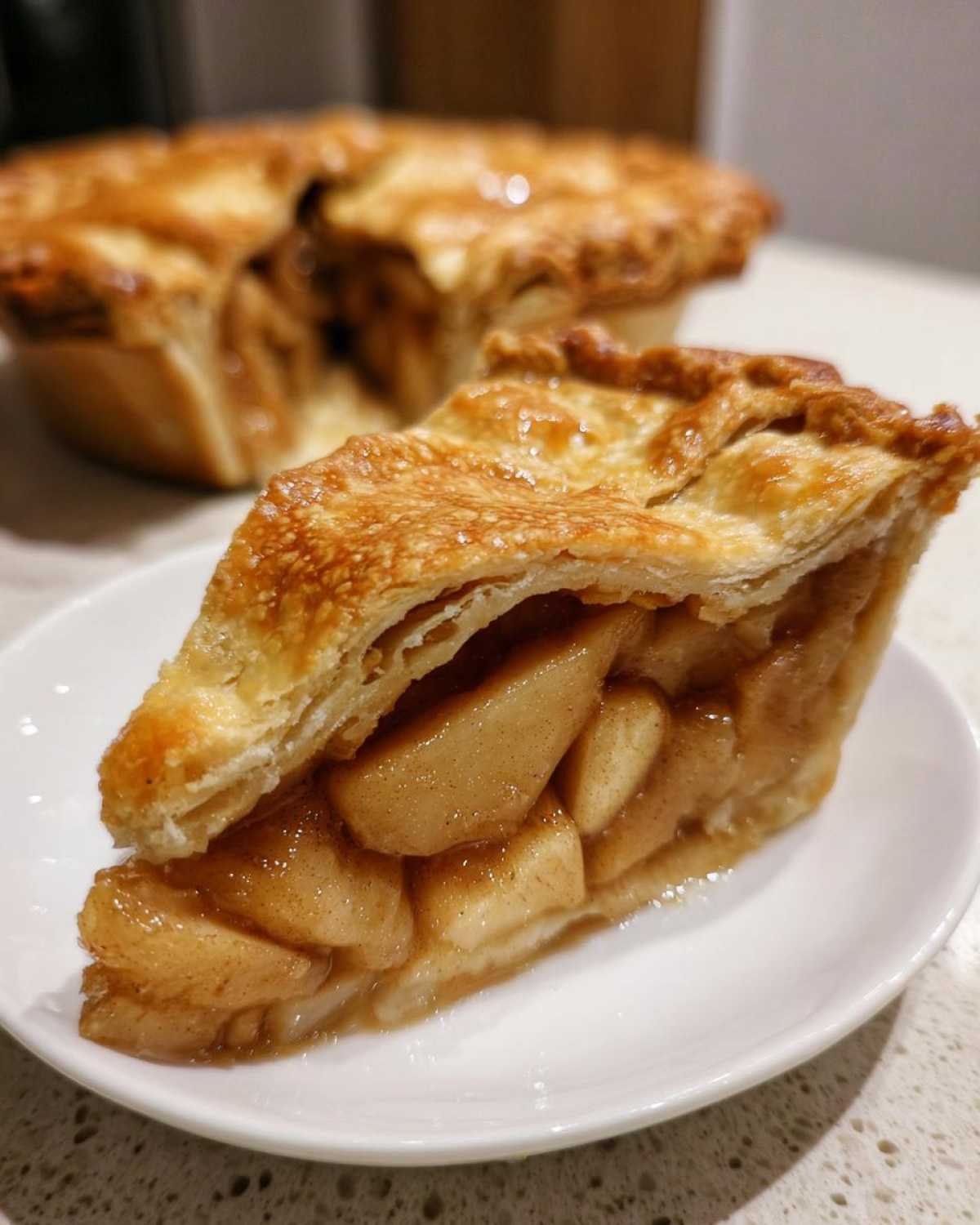 A close-up of a slice of apple pies showing thick, caramelized apple filling and a golden, flaky crust.