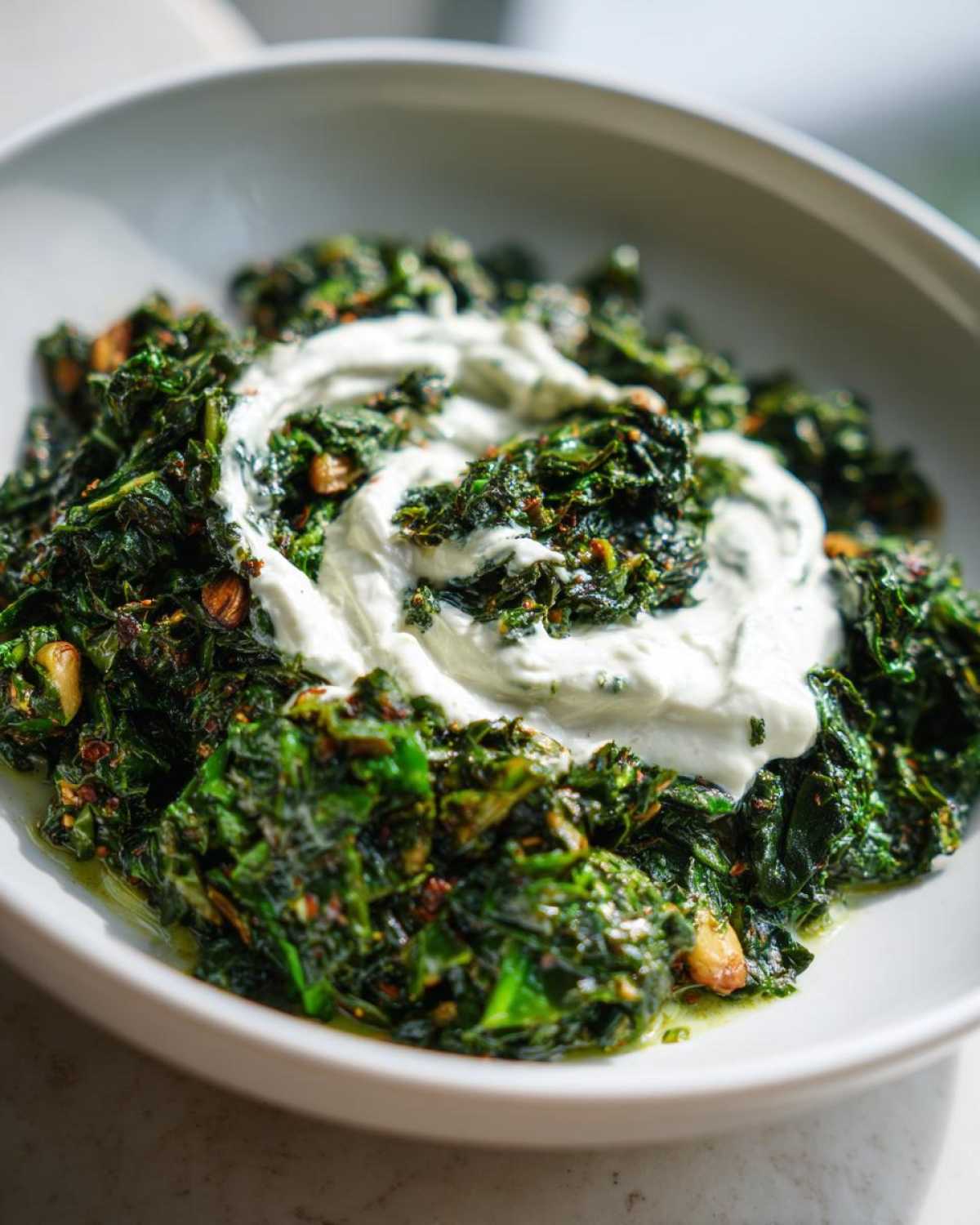 Close-up of cooked greens topped with a swirl of white yogurt, likely a component of persian noodle soup.