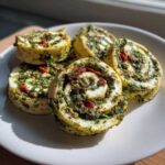 Five savory slices of Italian pinwheels filled with vibrant green pesto, sun-dried tomatoes, and nuts, arranged on a white plate.