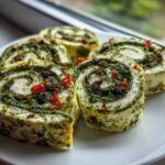 Four slices of creamy white and green pesto italian pinwheels appetizer served on a white plate.