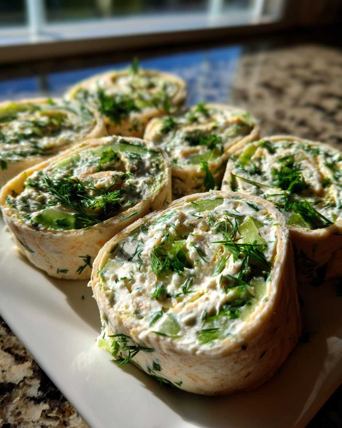 Several slices of Pickle Dip Pinwheels arranged on a white plate, showing creamy filling, chopped pickles, and fresh dill.