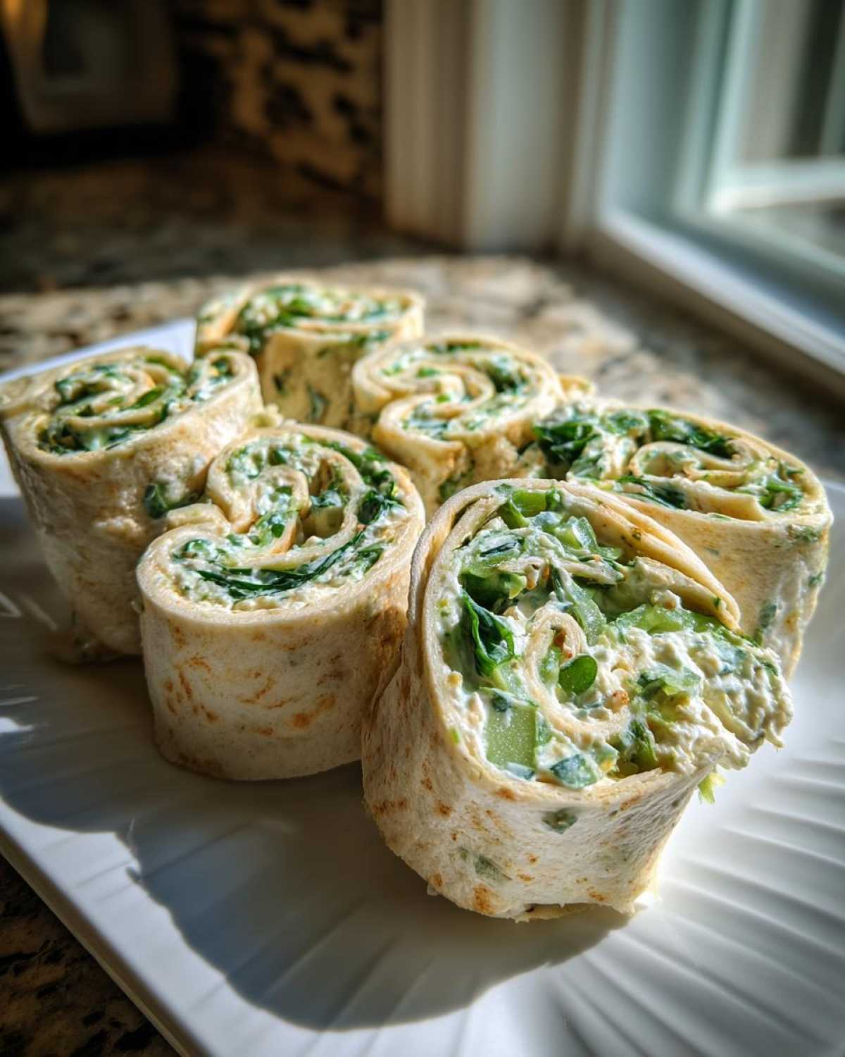 Close-up of several rolled Pickle Dip Pinwheels filled with creamy green mixture, served on a white plate.