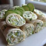 A platter of sliced Pickle Dip Pinwheels Favorite Blogger Recipes, filled with creamy dill mixture and cucumber chunks, garnished with fresh cucumber slices.