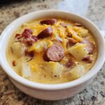 Close-up of a creamy Pioneer Woman Sausage Potato Chowder topped with shredded cheddar cheese and sliced sausage.