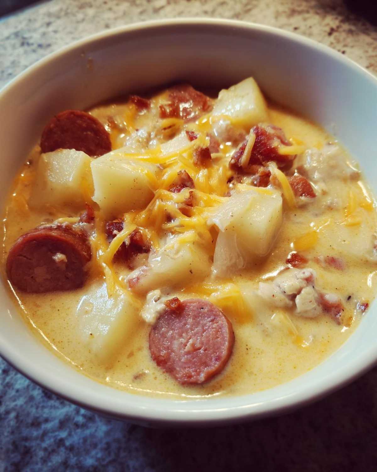 Close-up of a creamy bowl of Pioneer Woman Sausage Potato Chowder topped with shredded cheese and bacon bits.