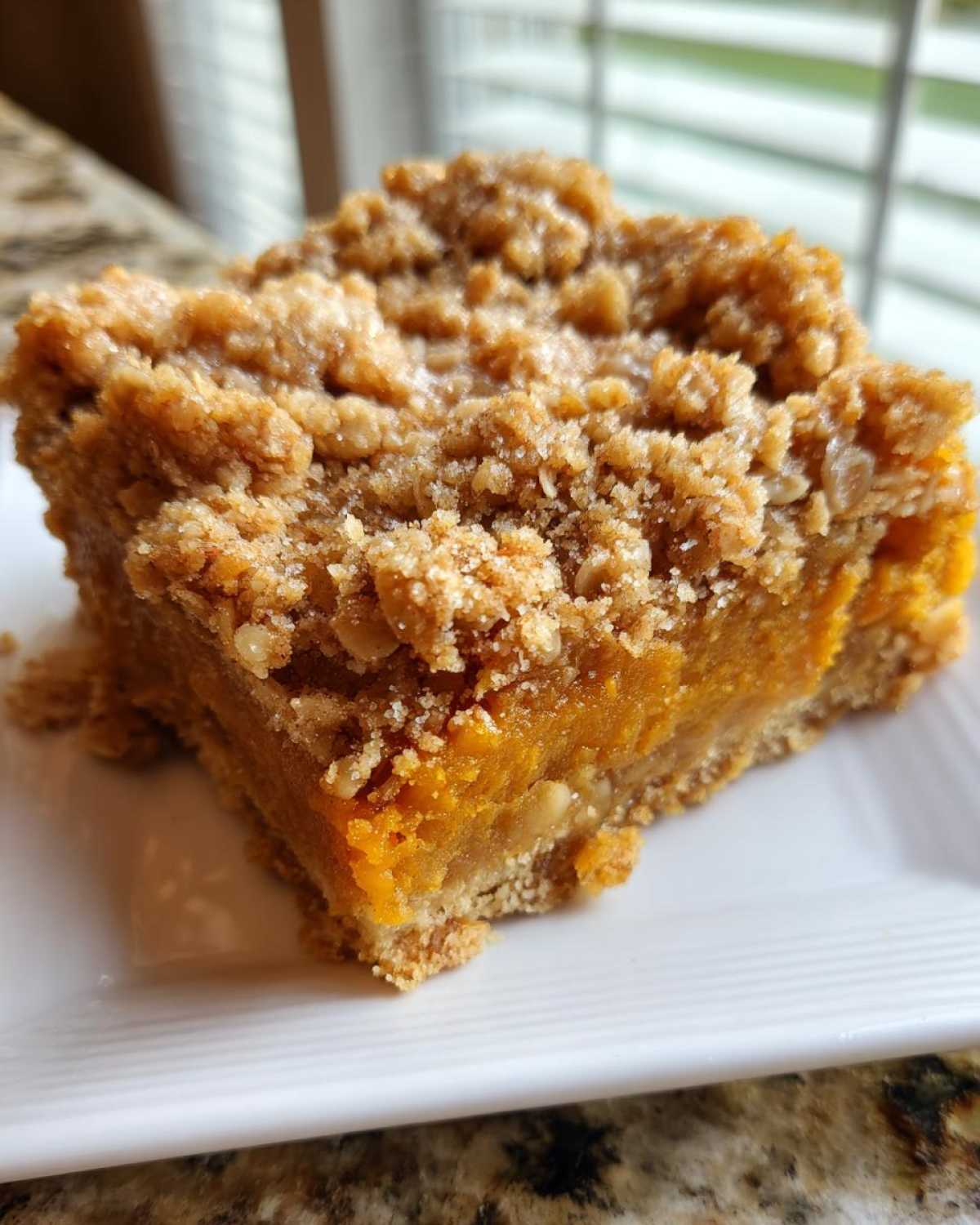 A close-up view of a thick square slice of pumpkin crisp bar with a rich orange filling and crumbly topping.
