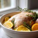 Raw turkey soaking in liquid with orange slices and herbs for turkey brine preparation.