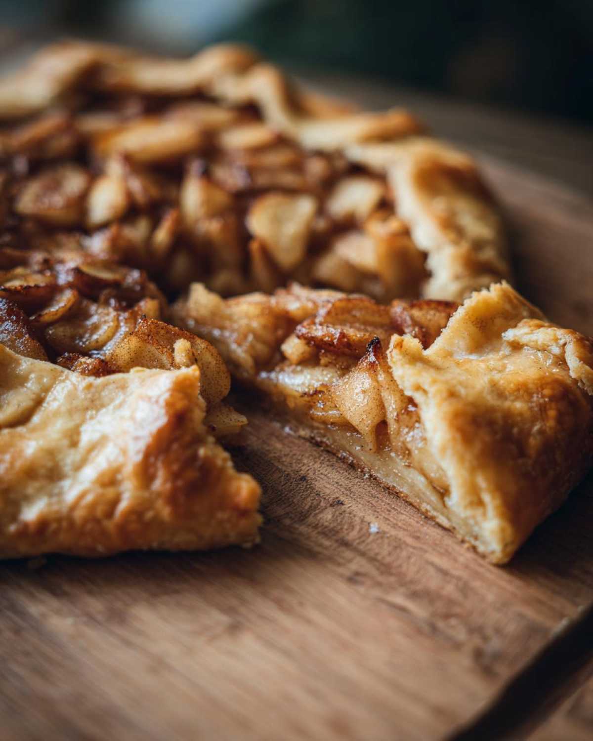 Close-up of a rustic apple galette with a slice cut out, showing caramelized apples and flaky crust.