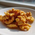 Close-up of a small pile of Savory Garlic Butter Chex Mix Crunchy Snack coated in seasoning on a white plate.