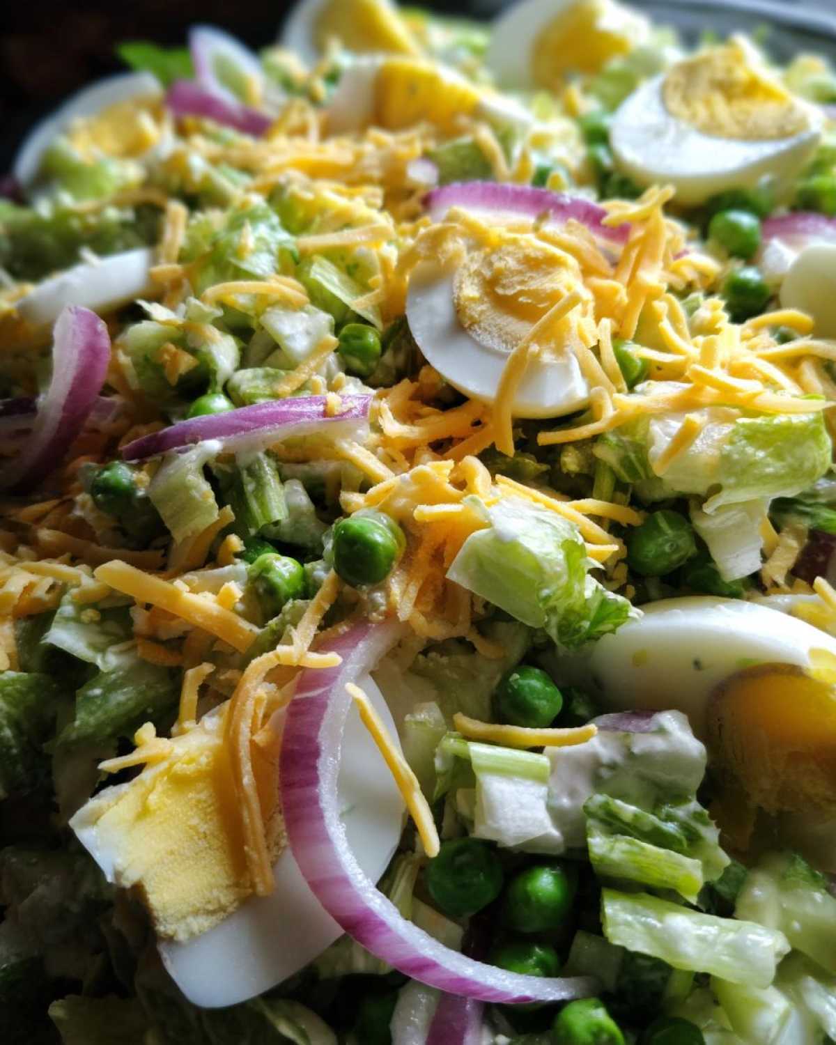 Close-up view of the top layer of a seven layer salad, featuring shredded cheese, sliced hard-boiled eggs, red onion, and peas.