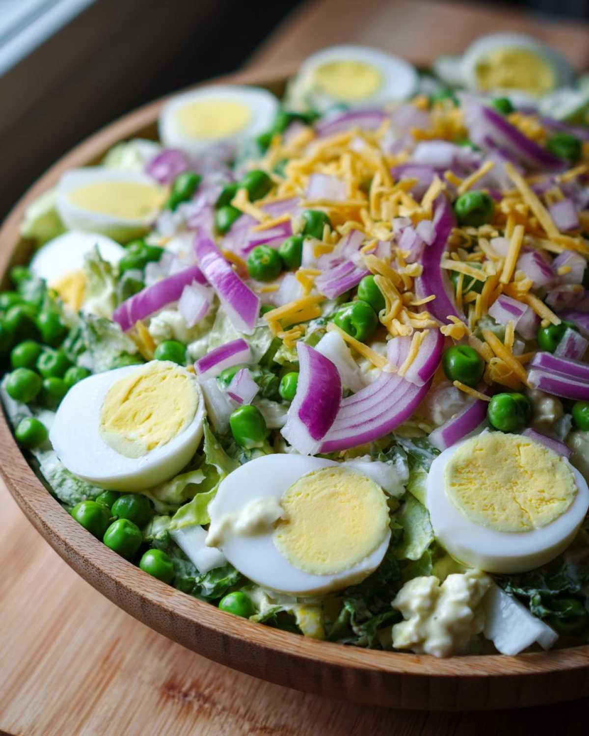 Close-up of the top layer of a seven layer salad featuring sliced hard-boiled eggs, red onion, peas, and shredded cheese.