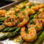 Close-up of juicy, seasoned shrimp and bright green asparagus on a sheet pan for Sheet Pan Crispy Garlic Butter Shrimp and Asparagus.
