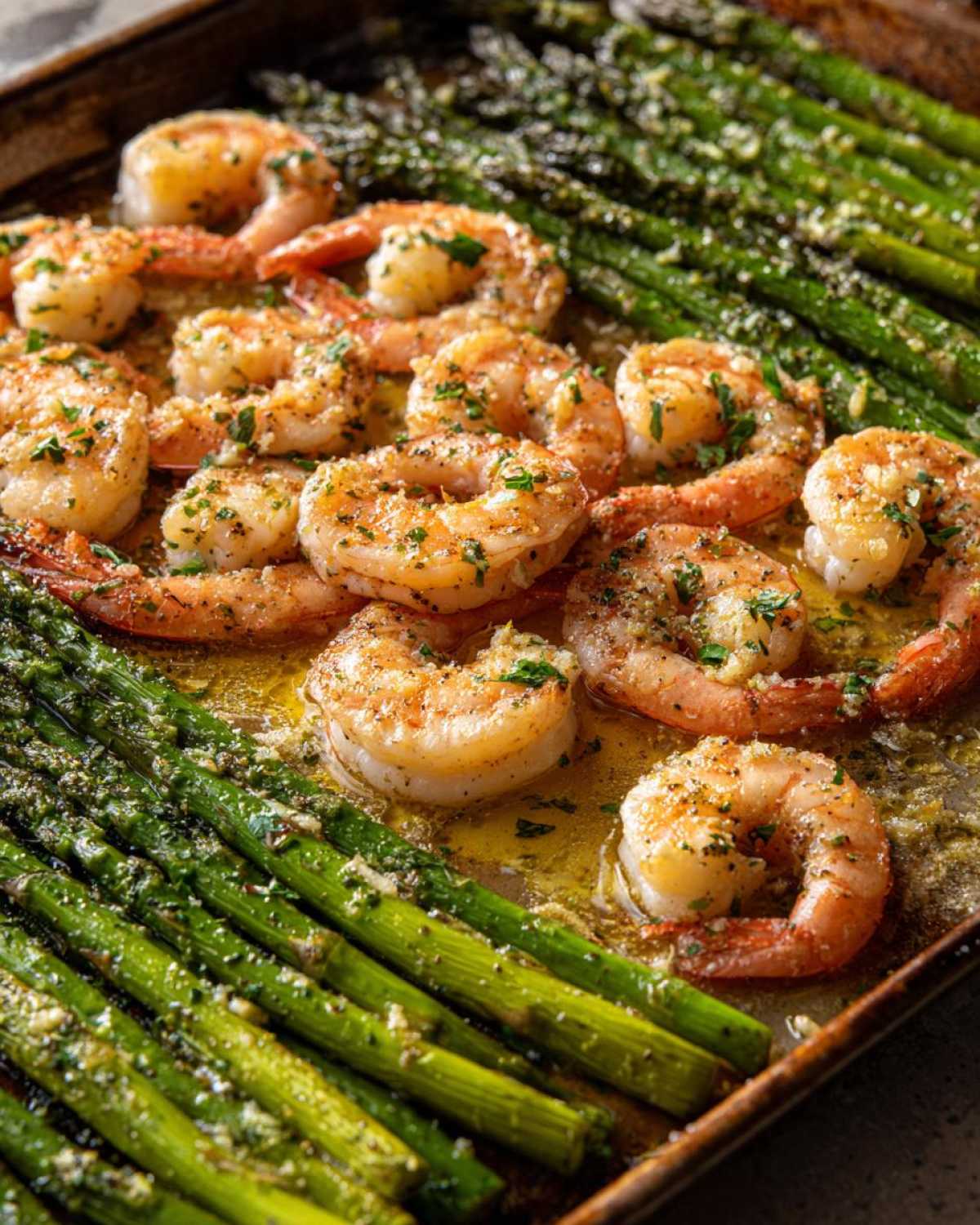 Close-up of Sheet Pan Crispy Garlic Butter Shrimp and Asparagus glistening in butter sauce on a baking sheet.