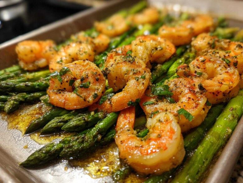 Close-up of juicy, seasoned shrimp and bright green asparagus on a sheet pan for Sheet Pan Crispy Garlic Butter Shrimp and Asparagus.