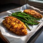 Two fillets of Sheet Pan Crispy Parmesan Tilapia served with a pile of bright green roasted green beans.