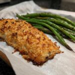 Close-up of Sheet Pan Crispy Parmesan Tilapia with Green Beans served on parchment paper.