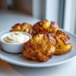 Close-up of crispy Sheet Pan Crispy Smashed Potatoes seasoned with herbs, served with a side of creamy garlic aioli.