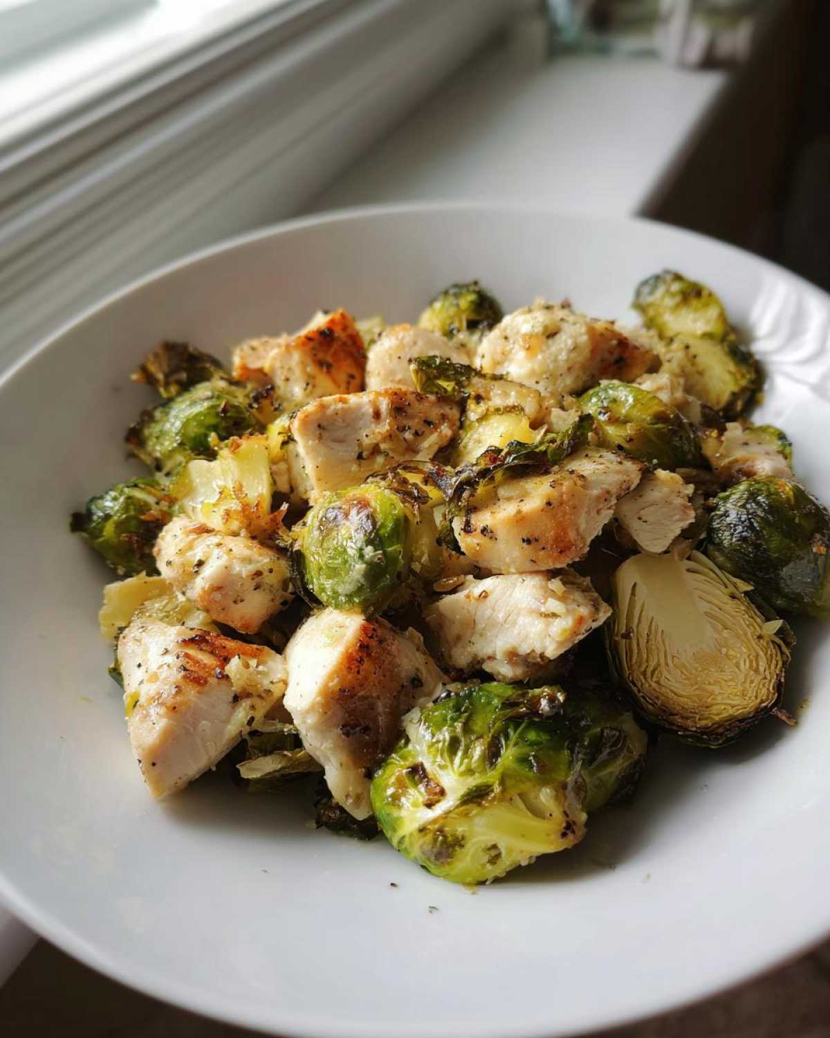 A white bowl filled with roasted chicken pieces and charred Brussels sprouts from the Sheet Pan Garlic Butter Chicken and Brussels Sprouts recipe.