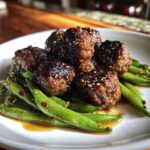 Close-up of glazed Sheet Pan Sticky Sesame Meatballs served over bright green snap peas.