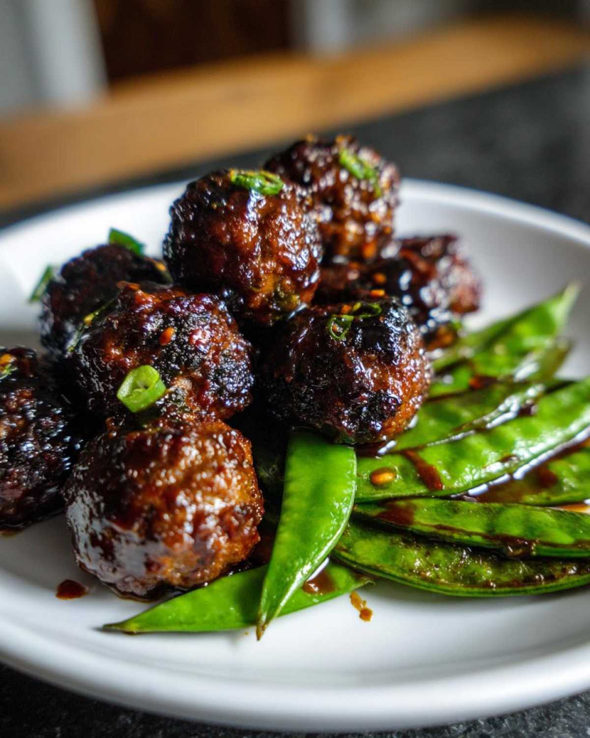 Close-up of glossy Sheet Pan Sticky Sesame Meatballs served over bright green snap peas.