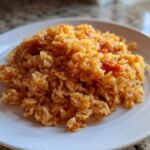 A close-up of a mound of Simple & Fluffy Mexican Rice on a white plate.