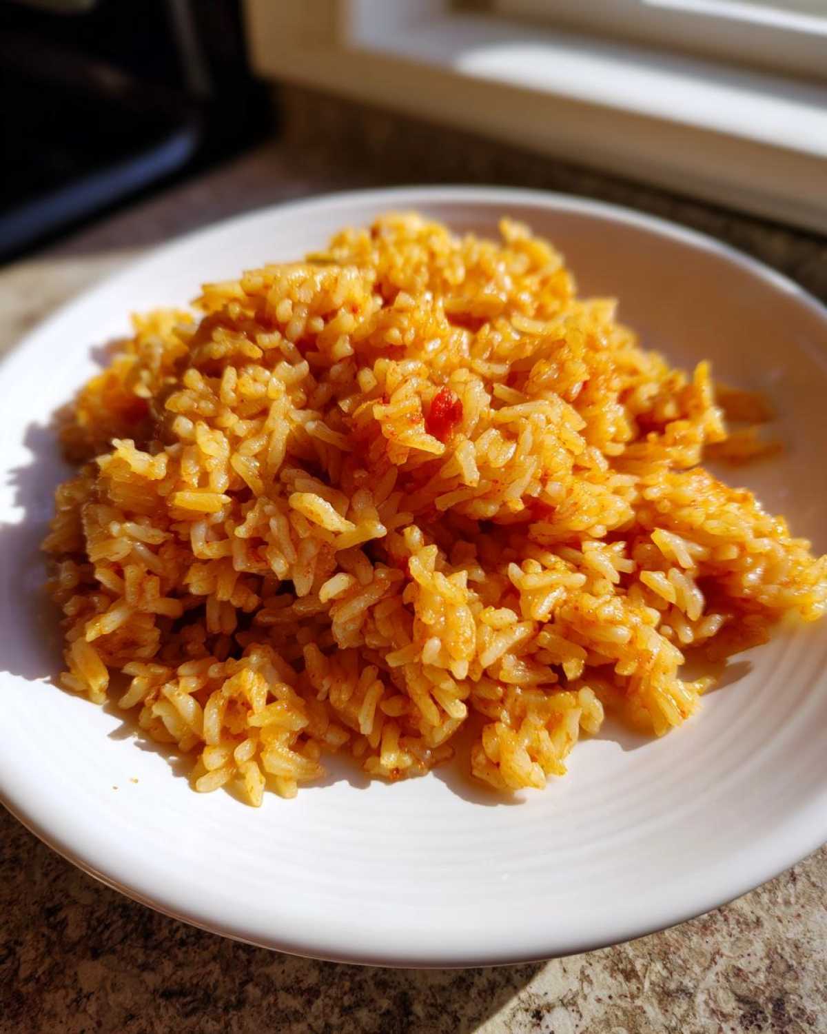 A white plate piled high with bright orange Simple & Fluffy Mexican Rice, illuminated by sunlight.