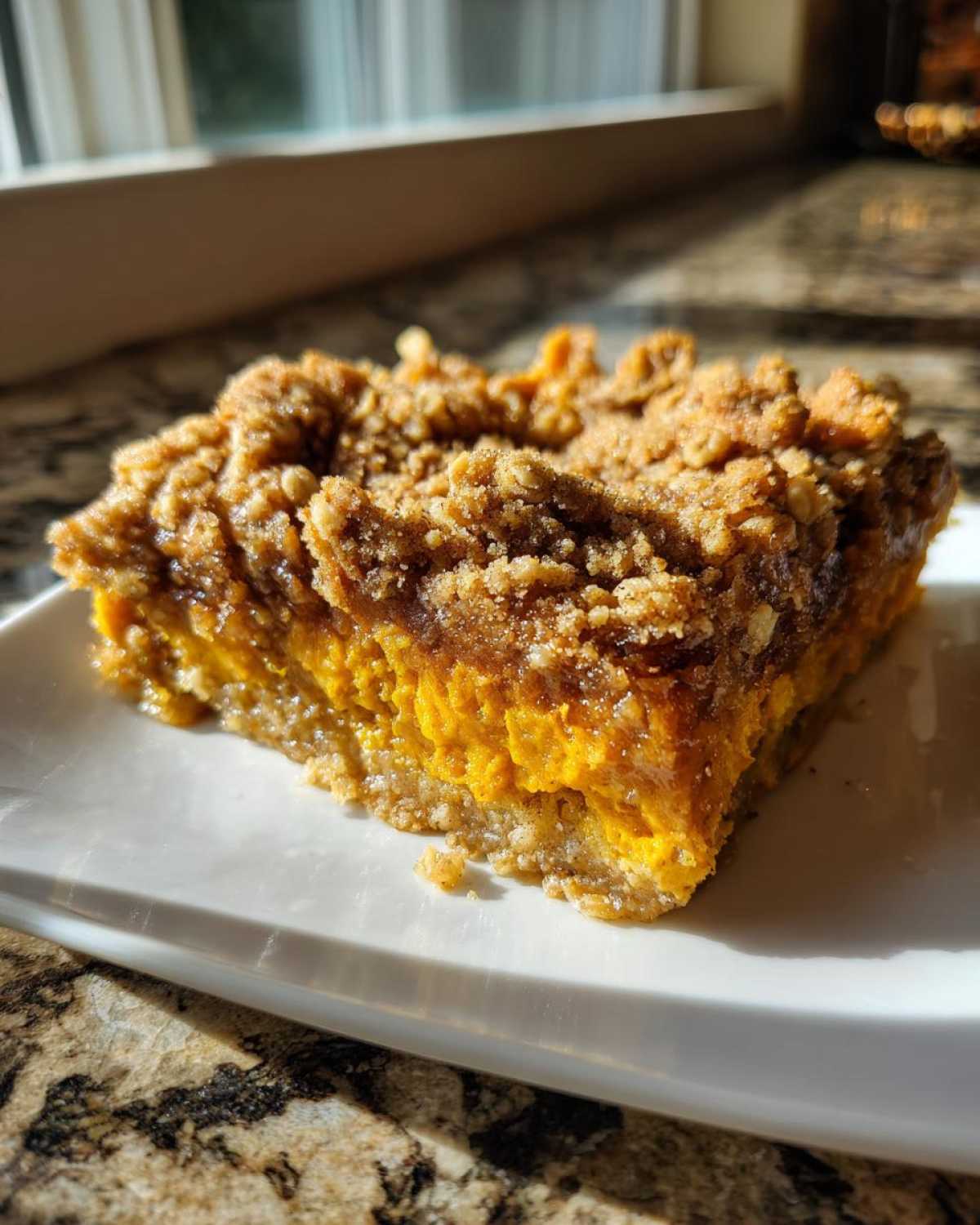 A square slice of rich, orange pumpkin crisp with a thick, crumbly topping served on a white plate.