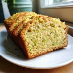 Close-up of a freshly baked loaf of Gluten-Free Lemon Zucchini Bread, sliced and showing moist texture with green zucchini shreds.