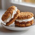 Close-up of two soft oatmeal cream pies stacked with thick white cream filling, lightly dusted with spice.