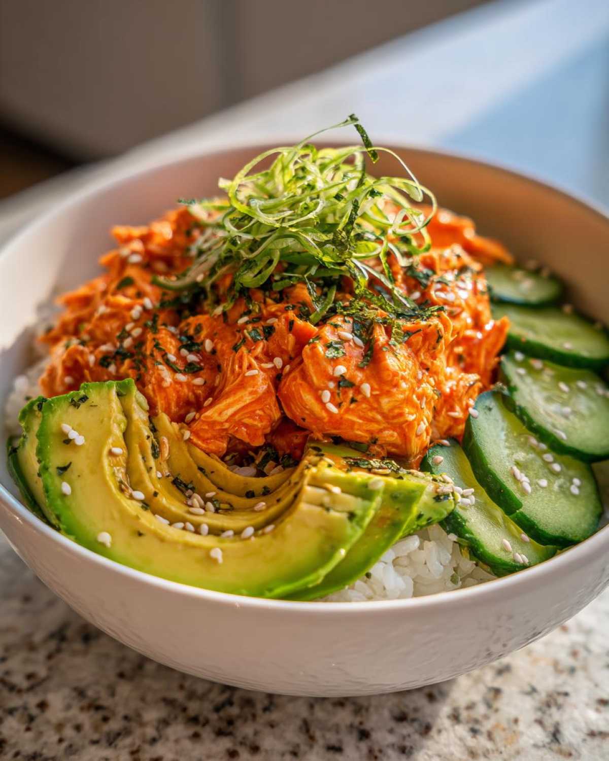 A close-up of a spicy crab sushi bowl featuring creamy orange spicy crab mix over rice, sliced avocado, and cucumber.
