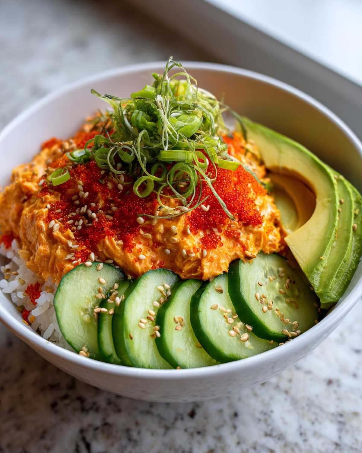 A close-up of a spicy crab sushi bowl featuring creamy orange crab mix, bright red tobiko, sliced cucumber, avocado, and green onions.