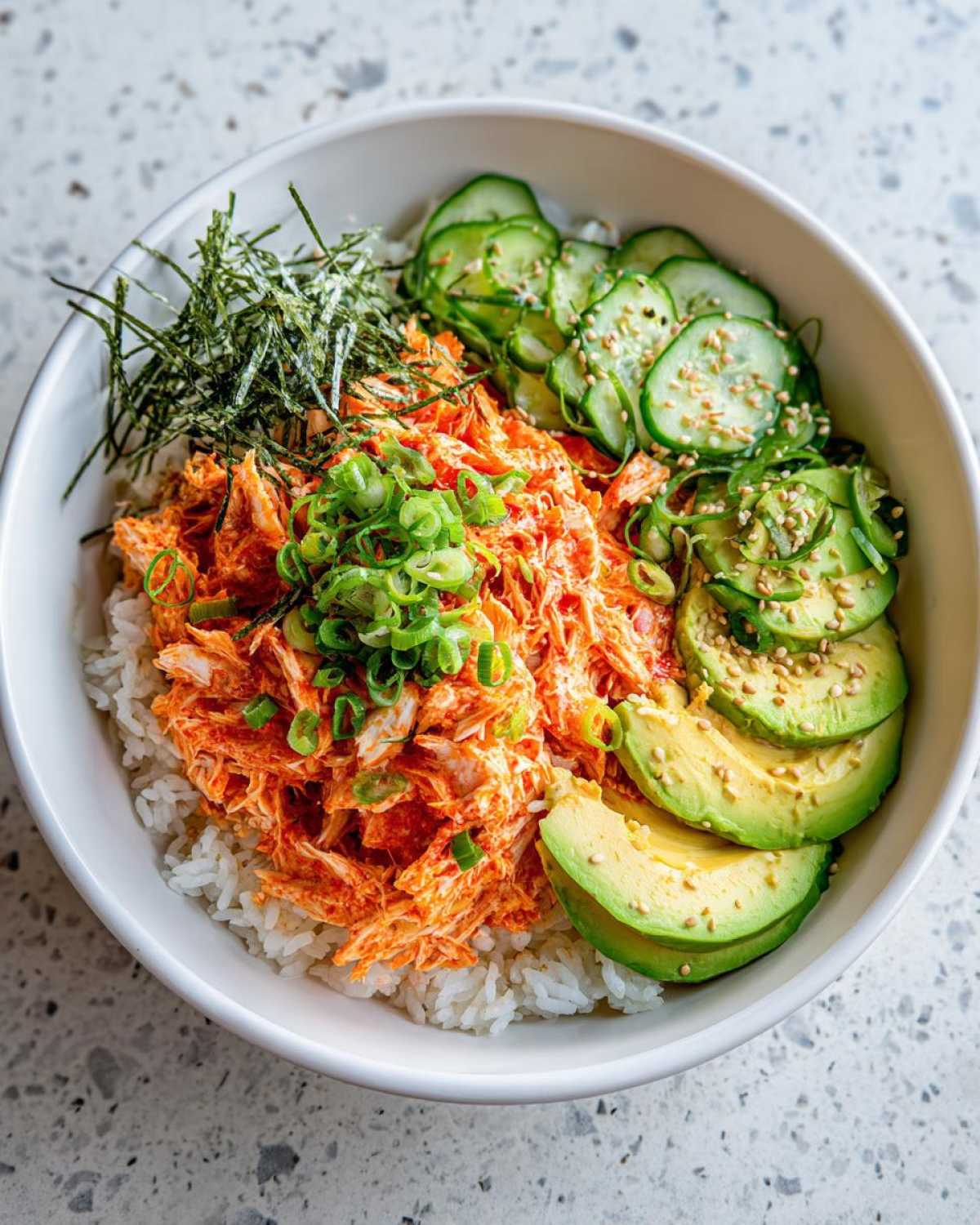 A vibrant spicy crab sushi bowl featuring shredded spicy crab mix over rice, topped with sliced avocado, cucumber, and nori.