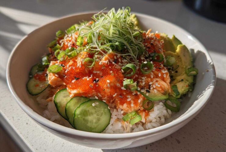 A vibrant spicy crab sushi bowl featuring rice topped with spicy crab mixture, bright orange tobiko, sliced avocado, cucumber, and green onions.