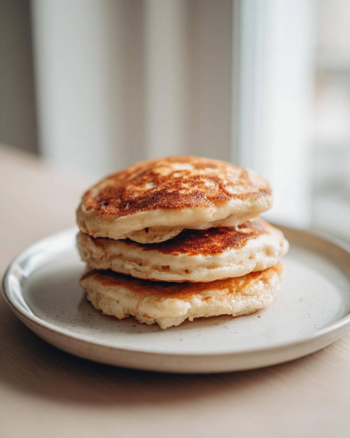 A stack of three golden-brown Banana Pancakes resting on a light speckled plate.