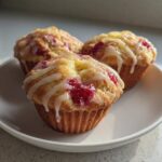 Three delicious Strawberry Yogurt Muffins topped with a white glaze, resting on a white plate.