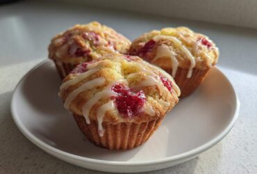 Three delicious Strawberry Yogurt Muffins topped with a white glaze, resting on a white plate.