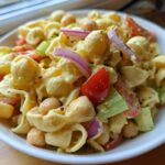 Close-up of Vegan Creamy Lemon Chickpea Pasta Salad with pasta shells, chickpeas, tomatoes, red onion, and celery.