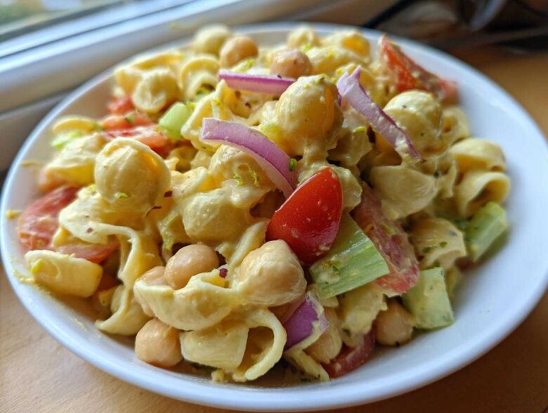 Close-up of Vegan Creamy Lemon Chickpea Pasta Salad with pasta shells, chickpeas, tomatoes, red onion, and celery.