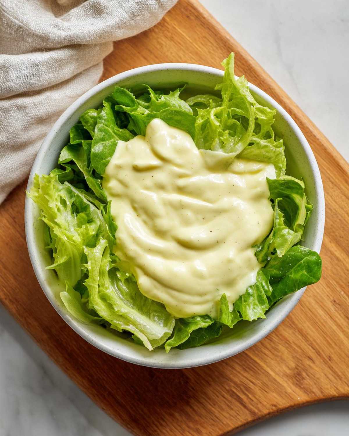A bowl of crisp lettuce topped with a generous dollop of Vegan Creamy Lemon Tahini Dressing.
