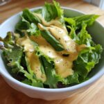 A white bowl filled with fresh green lettuce topped generously with Vegan Creamy Lemon Tahini Dressing.