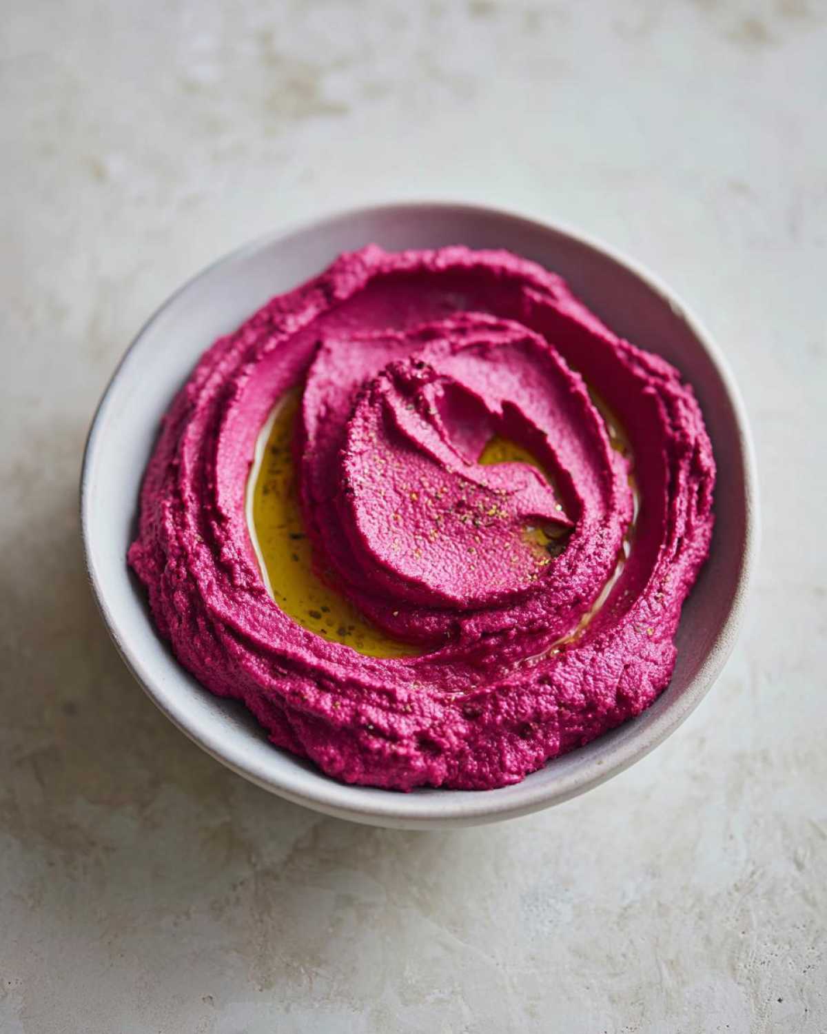 A bowl of vibrant pink Vegan Creamy Roasted Beet Hummus swirled and drizzled with olive oil.