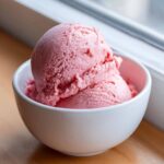 Two scoops of bright pink Vegan Creamy Strawberry Oat Milk Ice Cream in a small white bowl.