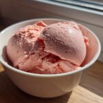 Two scoops of pink Vegan Creamy Strawberry Oat Milk Ice Cream in a white bowl.