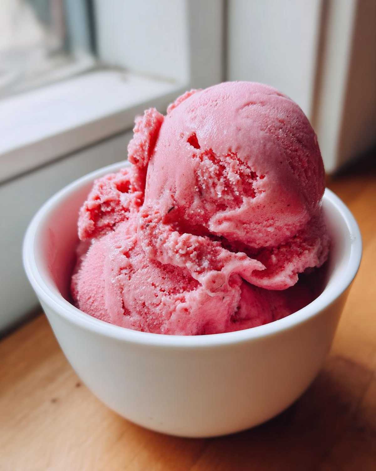 Close-up of two scoops of bright pink Vegan Creamy Strawberry Oat Milk Ice Cream in a white bowl.
