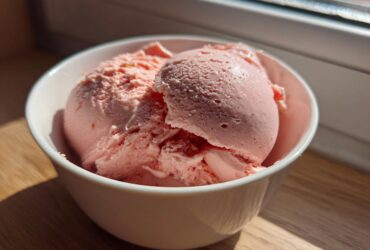 Two scoops of pink Vegan Creamy Strawberry Oat Milk Ice Cream in a white bowl.