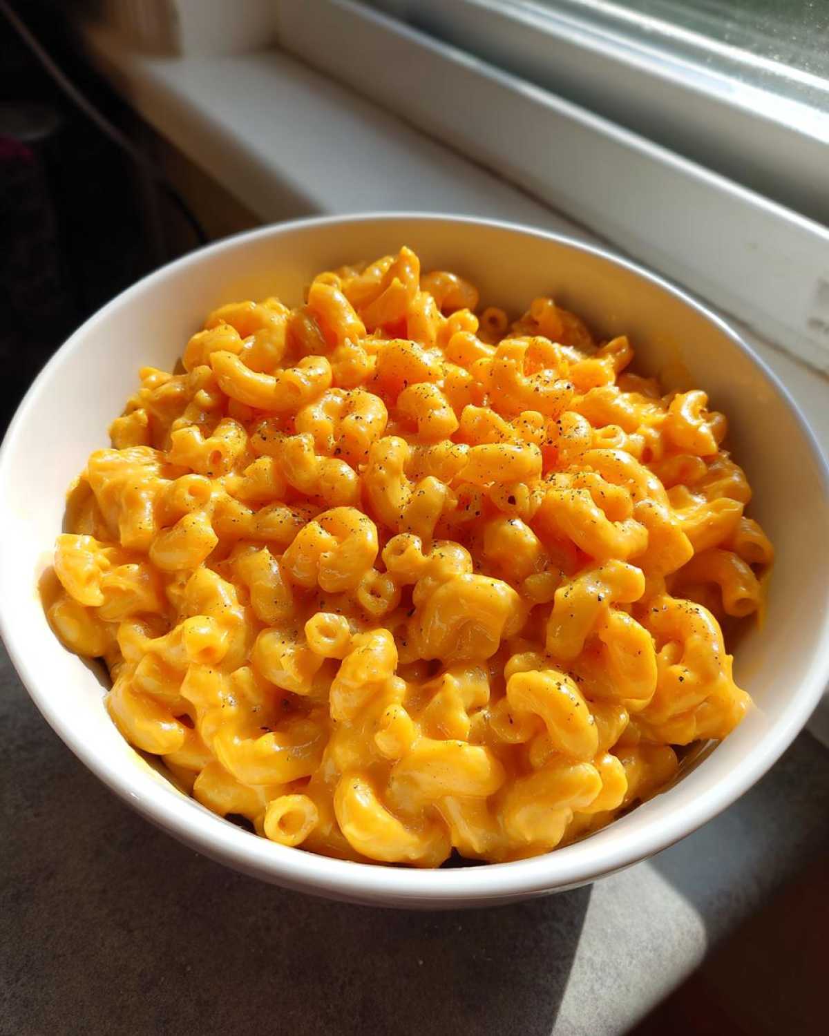 A white bowl filled with macaroni pasta coated in bright orange Vegan Creamy Sweet Potato Mac Sauce, sprinkled with pepper.