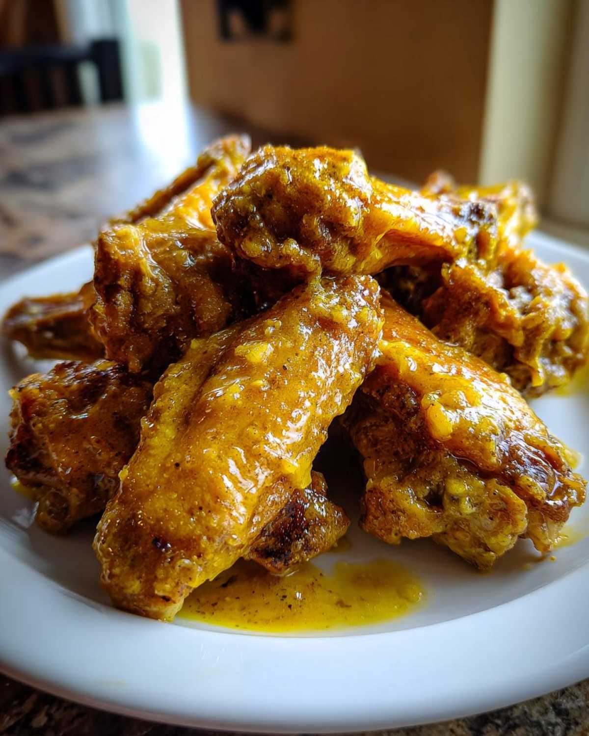 A pile of crispy chicken wings generously coated in a thick, glossy, yellow Copycat Garlic Parmesan Wing Sauce on a white plate.