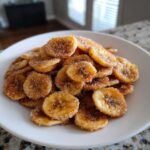 A white plate piled high with crispy Air Fryer Cinnamon Sugar Banana Chips coated in sweet cinnamon sugar.