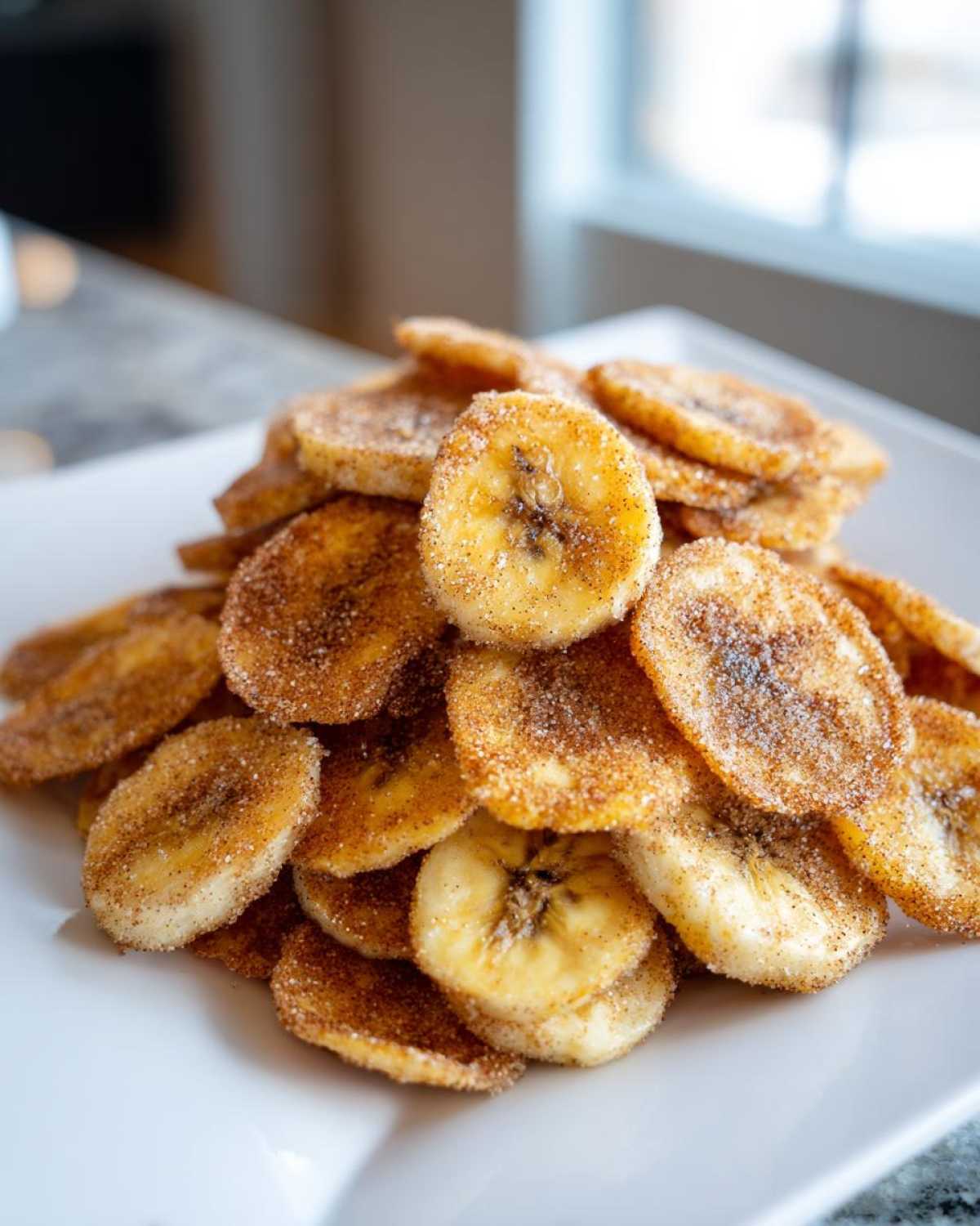 A close-up of a crispy pile of Air Fryer Cinnamon Sugar Banana Chips dusted heavily with cinnamon sugar.