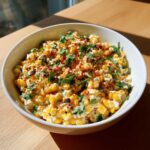 A white bowl filled with creamy Elote Dip, featuring corn kernels, white cheese, and topped with fresh cilantro and chili powder.